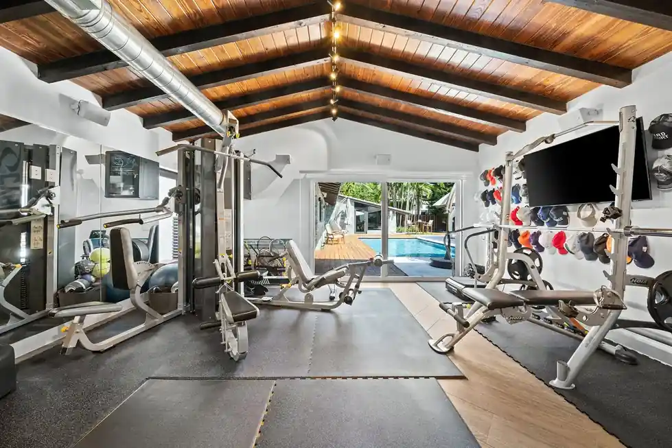 Casa Club home gym with weight machines, benches and a sliding glass door onto the pool deck