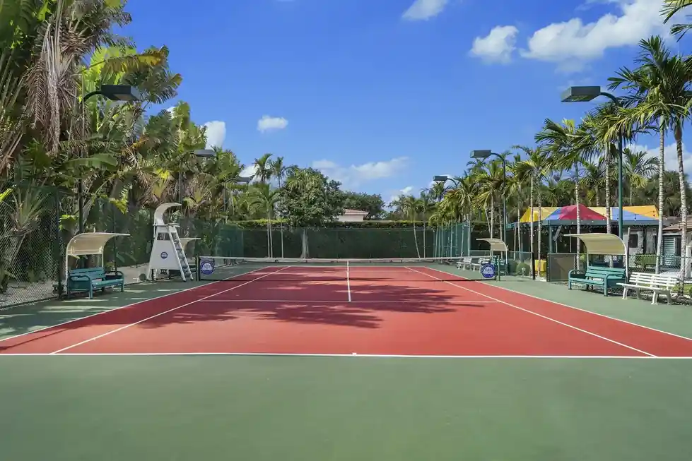Casa Club tennis court with a red surface, a green surround and an umpire chair, lined with palms