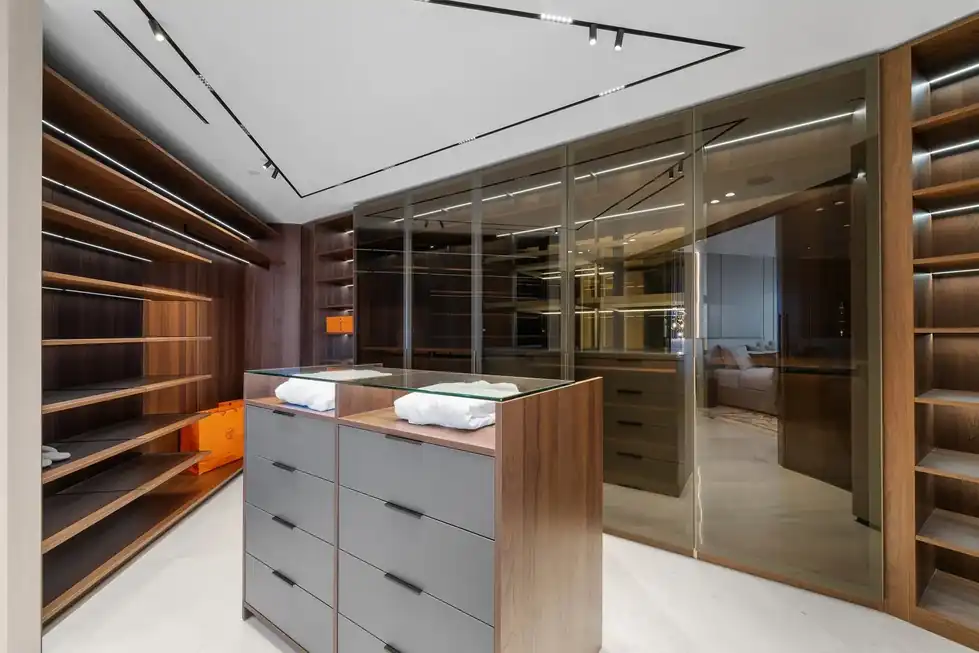 Lower PH66 walk-in closet with dark wood shelving, a glass-topped island and mirrored glass doors