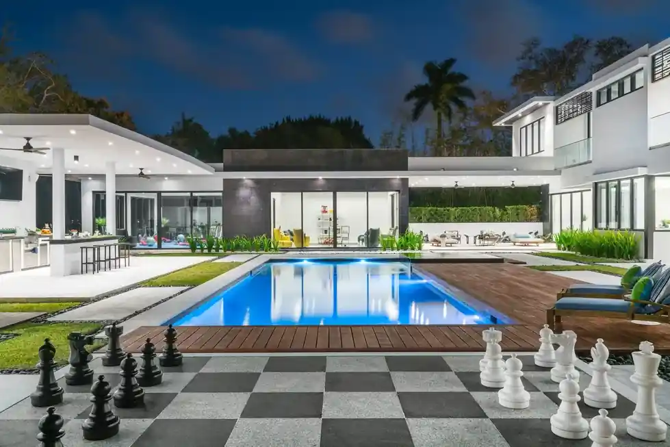 Casa Pinecrest at dusk: a checkered sundeck with giant chess pieces beside the lit pool